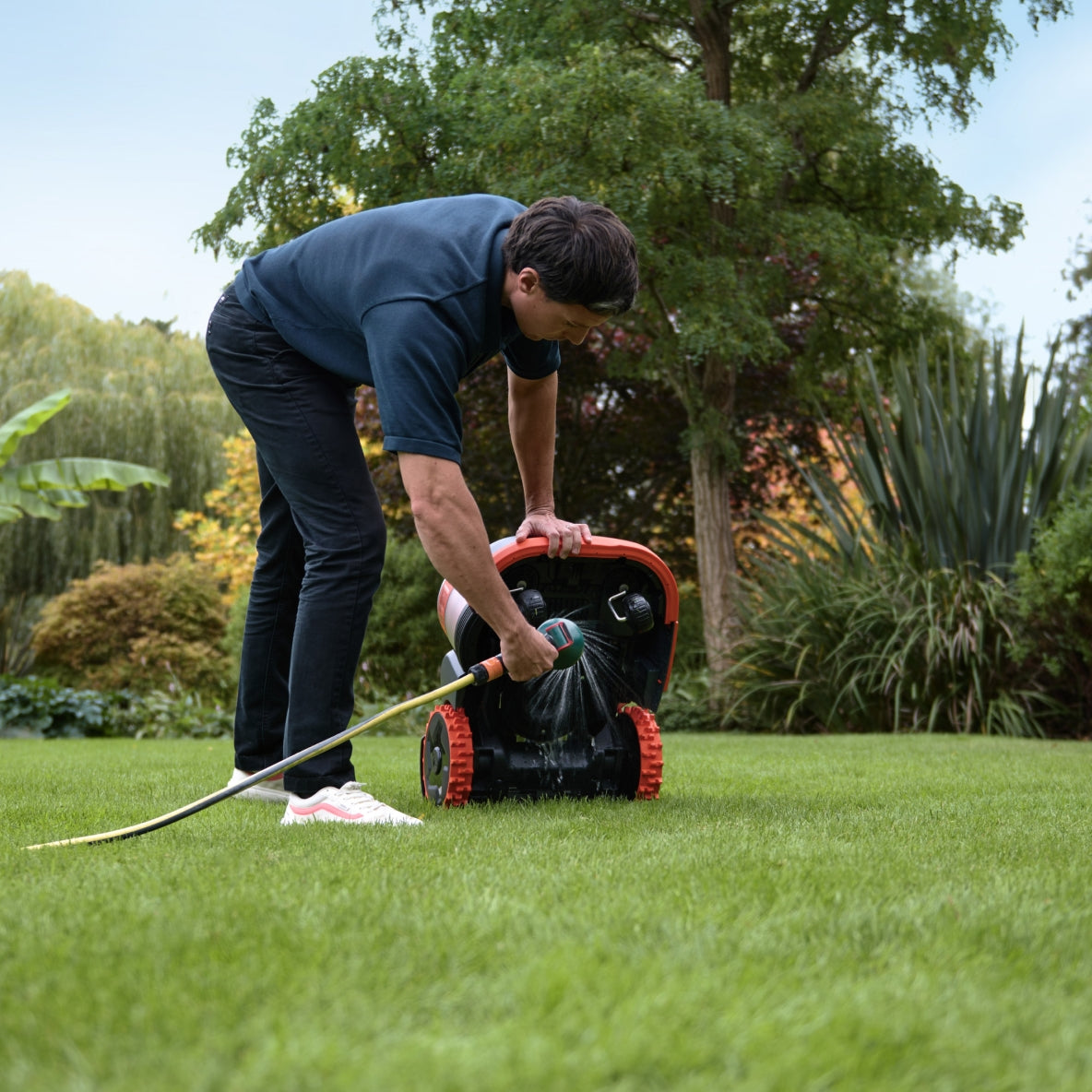 Man cleaning Navimow i110E robot lawn mower with a hose.